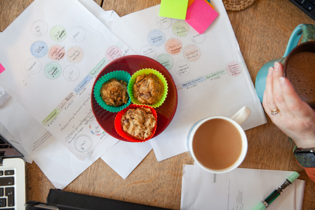 muffins in colourful cases, cups of tea and paperwork on a table.