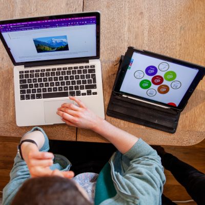 A person sitting at a laptop and tablet on a table from above.